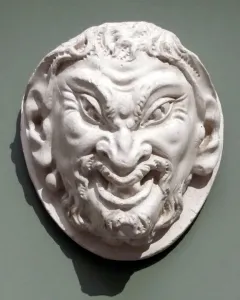 White circular relief sculpture of the Head of a Faun with a grinning face, pointed ears, and curly beard and hair.