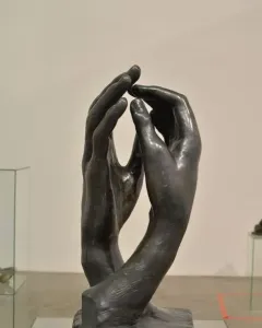The Cathedral sculpture showing two dark metal hands rising upright with fingertips nearly touching.