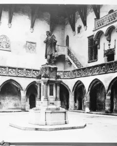 Copernicus Monument in a gothic courtyard, showing a robed statue holding a spherical instrument on a decorated pedestal.