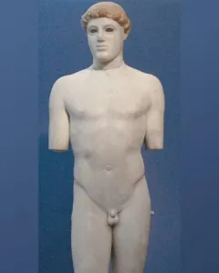 Kritios Boy marble statue of a nude young male figure against a blue background, missing its arms and part of one leg.