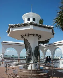 Mirador de la Flor monument with Selena Quintanilla statue, tribute plaque, and rose beside a bay railing.