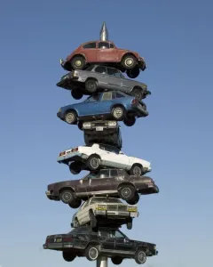 Spindle sculpture in Berwyn, Illinois, with eight cars stacked on a vertical spike against a clear blue sky.