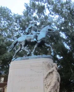 Stonewall Jackson equestrian statue on a stone pedestal surrounded by bushes and trees.