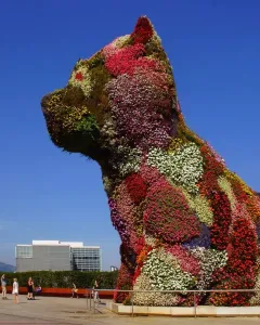 Jeff Koons’ Puppy topiary sculpture covered in flowers, with a skyscraper and city buildings behind it.