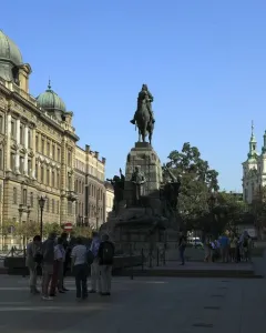 Grunwald Monument with an equestrian statue on a stone pedestal in a city square, with historic buildings and people nearby.