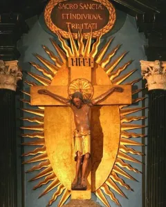 Gero Cross with a dark carved Christ figure on a golden crucifix, framed by Latin inscriptions and a sunburst backdrop.