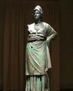 Minerva d\'Arezzo, a green-patinated armored figure standing on a wooden pedestal against a dark backdrop.