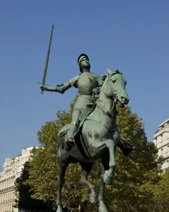 Joan of Arc equestrian statue in medieval armor holding a raised sword on a stone pedestal in Paris.