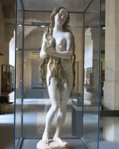 Mary Magdalene sculpture of a standing female figure with long wavy hair, displayed in a glass case.