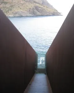 Steep rust-colored metal staircase descending between tall walls at the Walter Benjamin Memorial in Portbou.