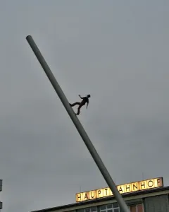 The Man Walking to the Sky sculpture rises on a tilted pole in a plaza in front of the main station buildings.