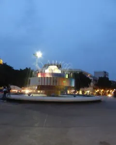 Fire and Water Fountain illuminated in a city square at dusk, with colorful vertical panels and arcing water jets.