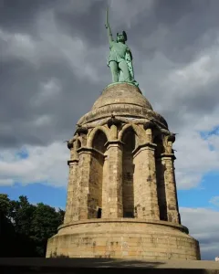 Hermannsdenkmal monument with a warrior statue holding a sword aloft against a dramatic cloudy sky.