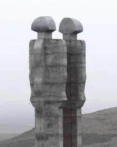 Two colossal abstract concrete figures of the Monument to Humanity stand on a hillside with scaffolding between them and two people at the base.