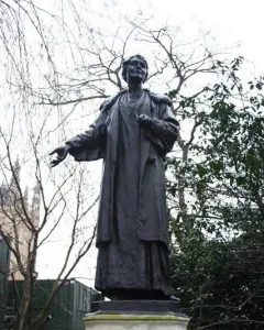 Pankhurst Memorial statue on a tiered stone pedestal, with the figure’s arm outstretched outdoors among bare trees.