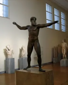 Artemision Bronze statue of a nude, bearded man with outstretched arms in a museum gallery.
