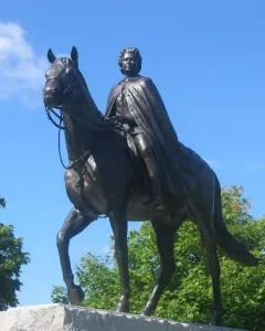 Elizabeth II equestrian statue on a stone pedestal with green foliage and blue sky behind it