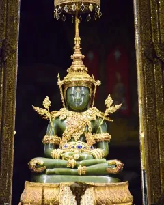The Emerald Buddha seated on a golden pedestal beneath an ornate canopy with gilded columns and jeweled decorations.
