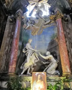 Noli Me Tangere sculpture showing a robed figure with an upraised hand facing a kneeling figure reaching out, set before a painted backdrop and framed by ornate columns.