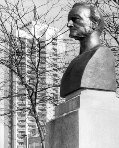 Richard Wagner bust on a stone base with his name carved into it, with bare branches and a tall apartment building in the background.