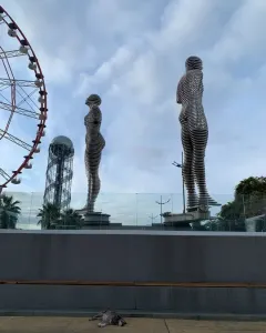 Ali and Nino sculpture with two slatted human figures facing each other, with a ferris wheel and spiral tower in the background.