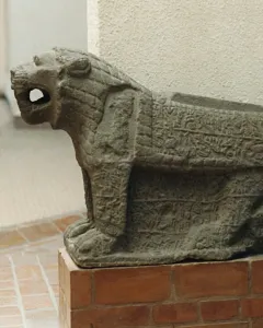 Maraş lion stone sculpture with an open mouth, carved in low relief and set on a brick pedestal.