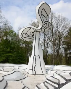 Jardin d\'émail sculpture with white abstract forms, black outlines, and tiered steps against trees and a cloudy sky.