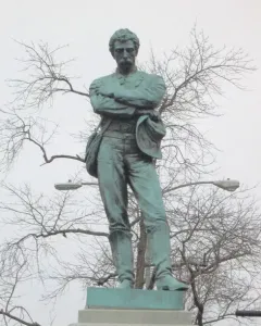 Appomattox bronze statue of a mustached man in military dress standing with arms crossed on a tiered stone pedestal.