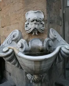 Fontana dello Sprone stone fountain with a carved bearded face spouting water into an ornate marble basin.