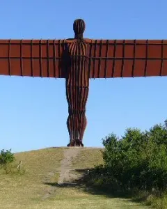 The Angel of the North sculpture stands on a grassy hill with outstretched wings under a clear blue sky.