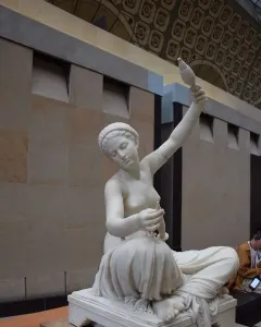 Jeune fille de Mégare, a white marble statue of a seated young woman spinning with a spindle and distaff.