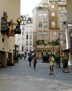 The Defender of Time clockwork sculpture on a building wall in Paris, showing a golden beast, a sphere, and a small sword-bearing figure.