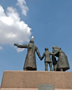 Auswandererdenkmal sculpture group on a tall granite pedestal, with a seagull perched on the central figure\'s head.