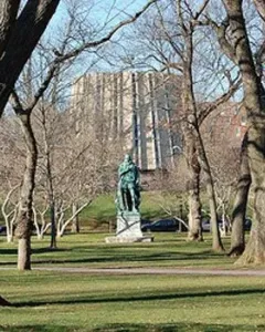 William the Silent bronze statue on a stone base in a grassy setting with leafless trees and a large building in the background