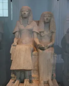 Horemheb and Amenia seated side by side on a stone bench, with their hands joined in the center.