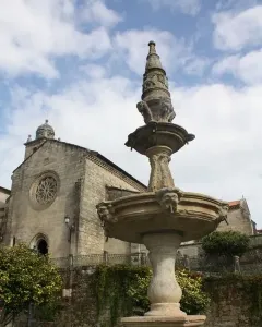 Herrería Fountain in a shallow green-tinged pool, with a stone building and rose window in the background.