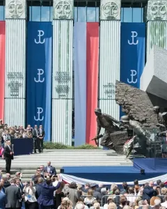 Warsaw Uprising Monument with a speaker addressing a crowd in front of it and Polish banners on a nearby building.