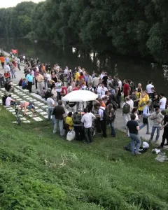Crowd gathered around the Keyboard Monument, a land-art installation made of rectangular blocks on a grassy slope beside the river.