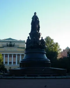 Catherine II Monument rising above a paved square under a clear blue sky, with a central figure and smaller seated figures on the pedestal.