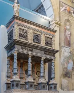 Martinengo Mausoleum with carved grey columns, a relief frieze, and small statues at the top inside a painted interior wall.