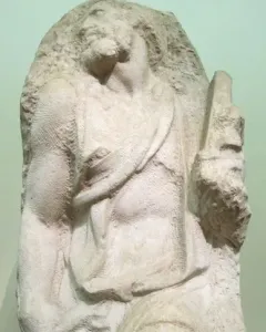 Saint Matthew sculpture carved from a rough stone block, with the figure emerging in a strained pose.