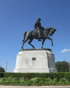 Gen. Beauregard equestrian statue on a tall stone pedestal, surrounded by hedges and flowers.