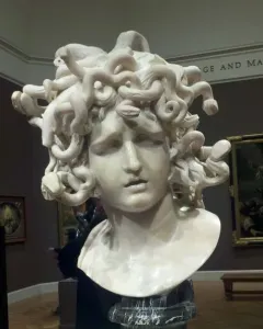Bernini\'s Medusa marble bust with snake-like hair and a sorrowful expression in a museum gallery.