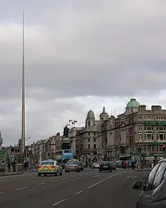 The Spire rises above Dublin street buildings under an overcast sky.