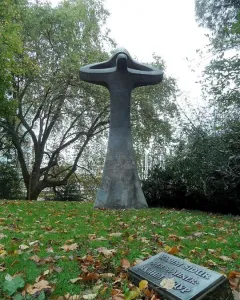 Der Mahner, a tall abstract bronze sculpture with upward-curving forms in a grassy park, with a plaque in front.