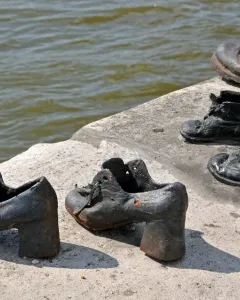 Metal shoes from the Shoes on the Danube Bank memorial on a concrete riverbank with calm water behind them.
