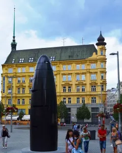 The Brno astronomical clock stands in a paved square with a yellow building and spire behind it.