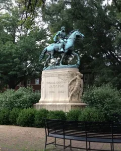 Stonewall Jackson equestrian statue on a stone pedestal surrounded by bushes and trees.