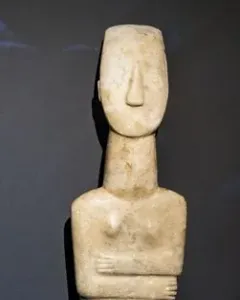 Cycladic marble female figurine with folded arms and a long neck.