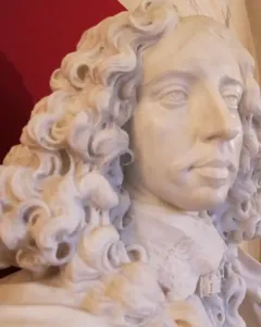 Marble bust of Francesco I d\'Este with curly hair, draped clothing, and an ornate pedestal against a black background.